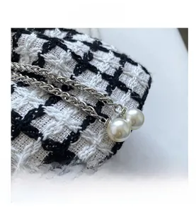 Detail view of black and white tweed woven bag with silver chain and pearl charms