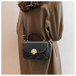 Close-up of black quilted crossbody bag with gold semicircular buckle and top handle