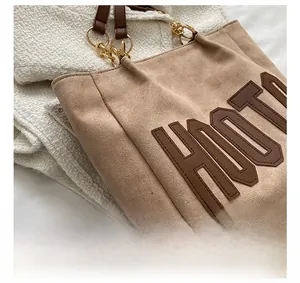 Detail of beige suede tote bag with brown letter patches and premium stitched leather straps