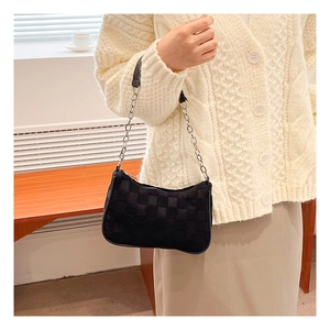 Detail of black checkered underarm bag with silver chain strap on a model's shoulder