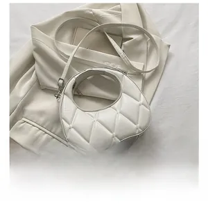 Detailed close-up of a white quilted crescent bag showing size compared to a smartphone