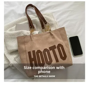 Detail view of large tote bag with letter patches showing size compared to a smartphone