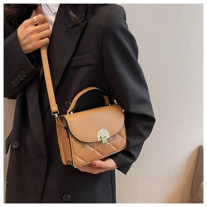 Detailed view of brown quilted crossbody bag with gold lock on black blazer model