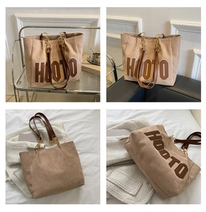 Detail of hooto letter embroidery on apricot suede tote bag with chain strap accents