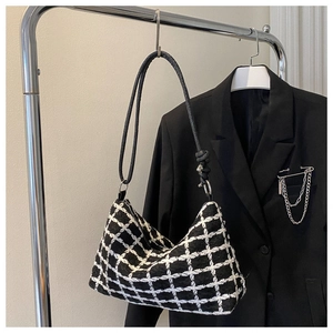 Close-up of black and white checkered tweed tote bag hanging on a minimalist boutique rack