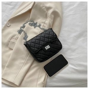 Detailed view of black quilted flap bag with silver turn-lock and chain strap