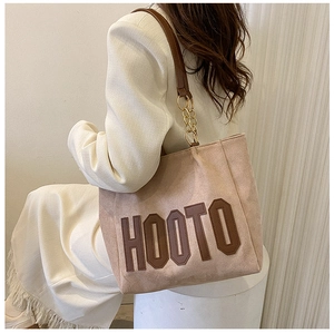 Detail of light beige tote bag with HOOTO lettering and gold chain shoulder strap