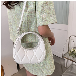 Detail of white quilted dumpling bag with silver hardware on a tweed suit model