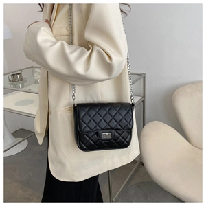 Detail of black quilted chain bag with silver twist lock on a minimalist outfit