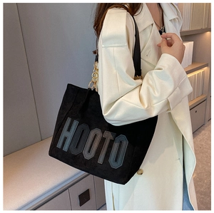 Side view of a large black suede tote bag with HOOTO logo and gold chain strap