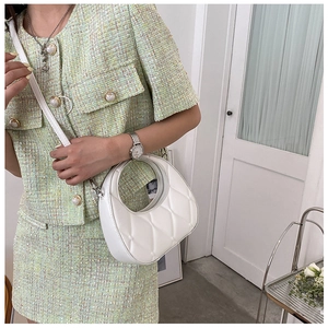 Detail of white quilted half-moon bag featuring round handle and chic metal buckle