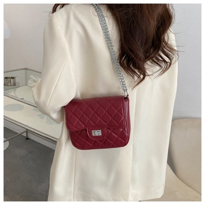 Burgundy quilted crossbody bag with silver chain strap worn by a model in a modern interior