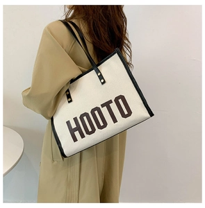 Vue latérale d'un grand sac cabas en toile avec lettres HOOTO et bordure noire sur modèle