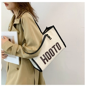 Sac fourre-tout en toile beige avec poignées noires porté avec un trench-coat élégant