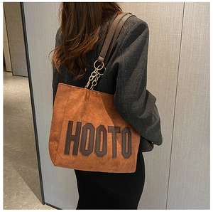 Detail of a large brown suede tote bag with bold letters and leather chain strap