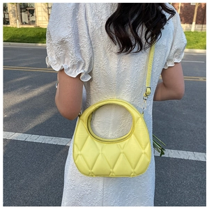 Detail view of bright yellow quilted dumpling bag with elegant leather shoulder strap