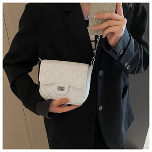 Close-up of white quilted crossbody bag with silver chain strap on black blazer