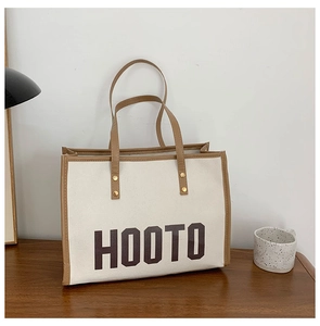 Détail du sac fourre-tout en toile avec anses en cuir marron et lettrage HOOTO sur table