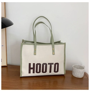 Détail du cabas en toile montrant le lettrage HOOTO et les attaches de poignée à rivets