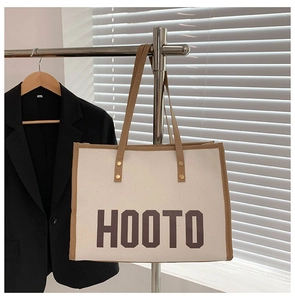 Détail du sac cabas en toile montrant la bandoulière en cuir marron et rivets en métal