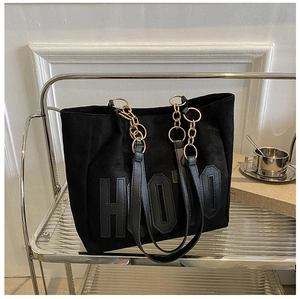 Detail of black tote bag with HOTO letter patch and gold chain strap on metal rack
