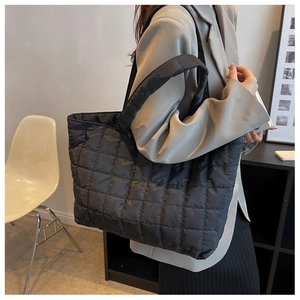 Side view of large black quilted tote bag with wide shoulder straps worn by model