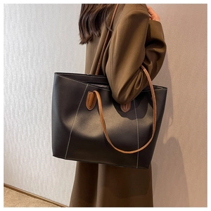 Side view of a large black faux leather tote bag with brown handles and contrast stitching