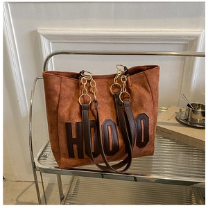 Close-up of brown suede tote bag with H000 lettering on a modern metal shelf