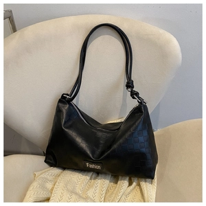 Detail of black faux leather handbag with checkered pattern and knot handle on a chair