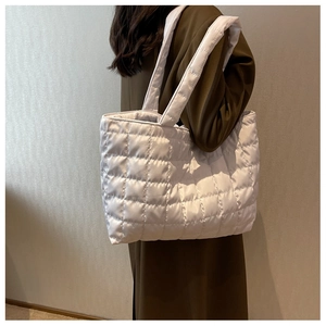 Quilted white puffy tote bag shown on shoulder of model wearing a trench coat