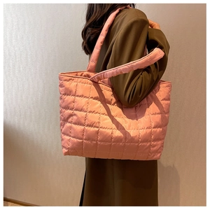 Detail of pink quilted nylon tote bag with thick shoulder straps on a brown coat