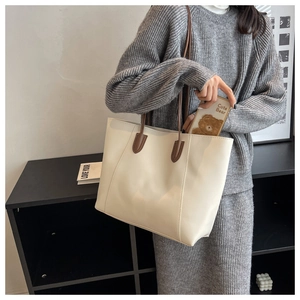 Detail of off-white tote bag with brown straps being used by a model in a grey sweater