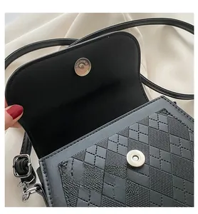 Detail of silver magnetic closure on a black quilted crossbody bag with flap open
