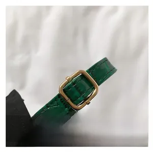 Detail of emerald green crocodile embossed faux leather strap with gold buckle adjustment