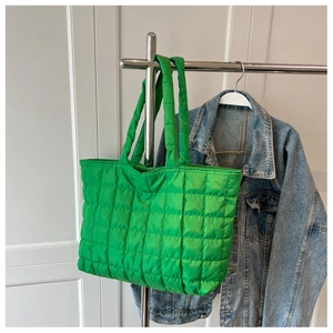 Detail of green quilted tote bag showing padded nylon texture and long shoulder straps