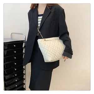 Dettaglio della borsa beige trapuntata con catena dorata indossata da modella in blazer nero