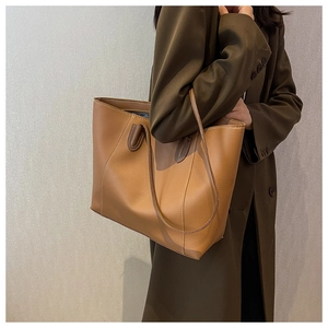 Detailed view of a brown leather tote bag with white stitching on a model's shoulder
