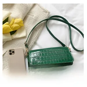 Detail of dark green crocodile texture shoulder bag with smartphone for size reference