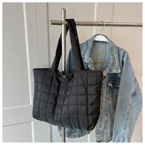 Detailed view of a black quilted puffer tote bag hanging on a rack with a denim jacket