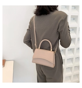Detail of beige crocodile pattern bag with woven handle shown from a side view