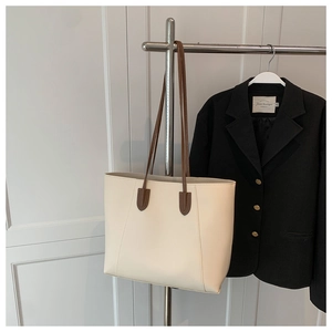 Detail view of cream leather tote bag with slim brown straps on a metal hanger