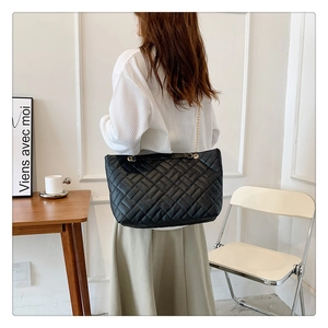 Grande borsa shopper trapuntata nera con catena dorata indossata da una modella