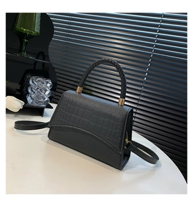 Detail of black faux crocodile leather handbag featuring an elegant woven handle and gold hardware
