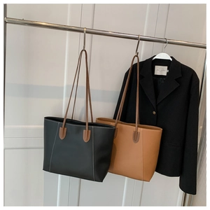 Detail of contrast stitching on black and brown leather tote bags hanging on a rack