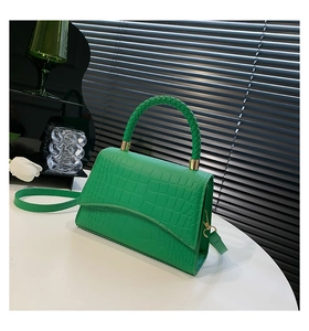Detail of green crocodile texture handbag with woven handle and gold metal hardware