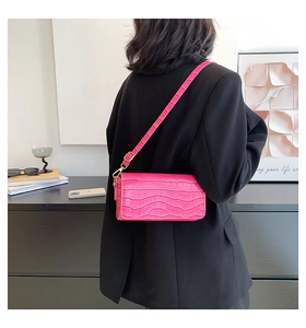 Detail of hot pink baguette bag with crocodile texture and gold hardware on model