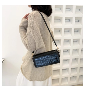 Detail of black crocodile embossed baguette bag with sleek shoulder strap and gold hardware