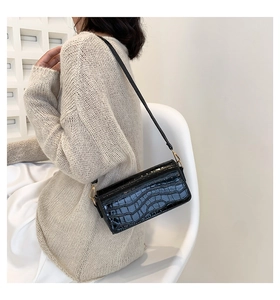 Close-up of black crocodile pattern baguette bag with gold hardware on beige knitwear