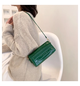 Detail of a dark green crocodile embossed baguette bag worn over a beige sweater