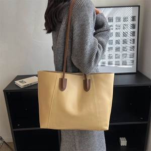 Large beige leather tote bag with dark brown straps worn by model in a modern interior
